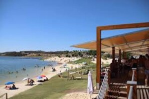 A beachside area with a covered seating area, umbrellas, and a view of the beach and sea.