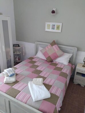 Cama bem arrumada com colcha xadrez, travesseiros e toalhas dobradas sobre um estrado branco.
