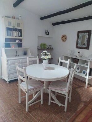 Uma sala de jantar com uma mesa redonda branca e quatro cadeiras, um armário branco com louças e um espelho na parede.