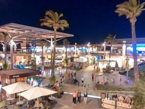 A bustling outdoor plaza with palm trees, seating areas, and a modern architectural structure. - 2Bed Apartment - Sleeps 5 - Pool, Parking, Pets (BENFERRI)