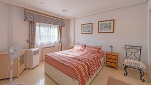 A bedroom with a bed, bedside tables, a chair, a radiator, and a window with curtains. - 2Bed Apartment - Sleeps 5 - Pool, Parking, Pets (BENFERRI)
