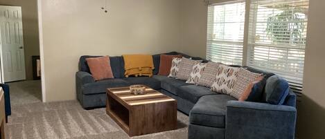 A living room with a sectional sofa, a wooden coffee table, and a carpeted floor.