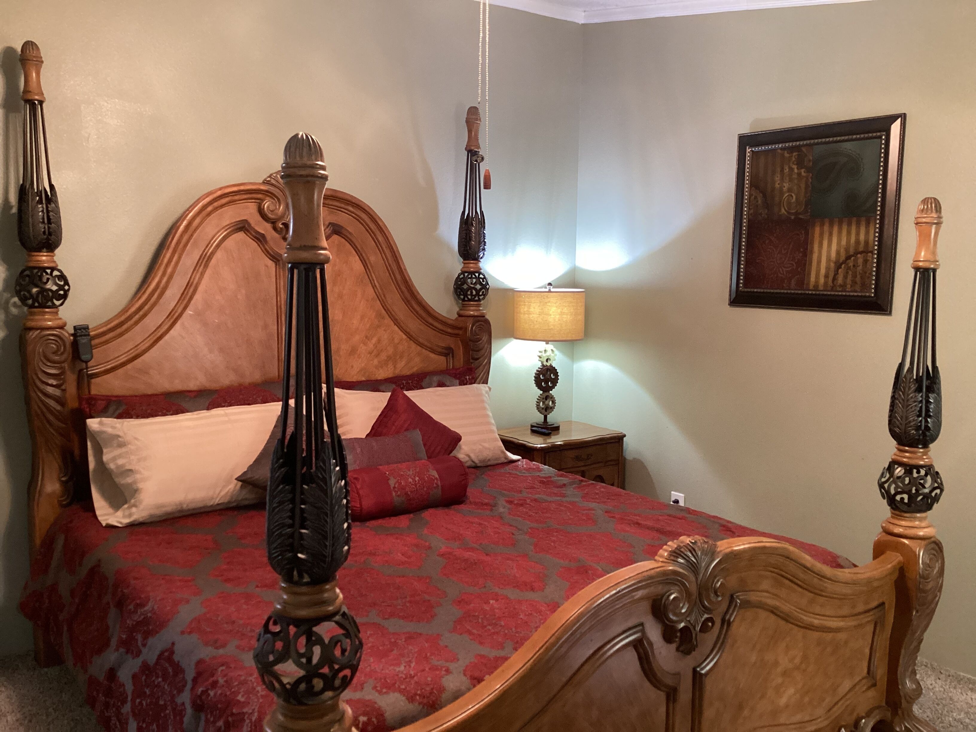 A bedroom with a four-poster bed, a nightstand with a lamp, and a framed picture on the wall.