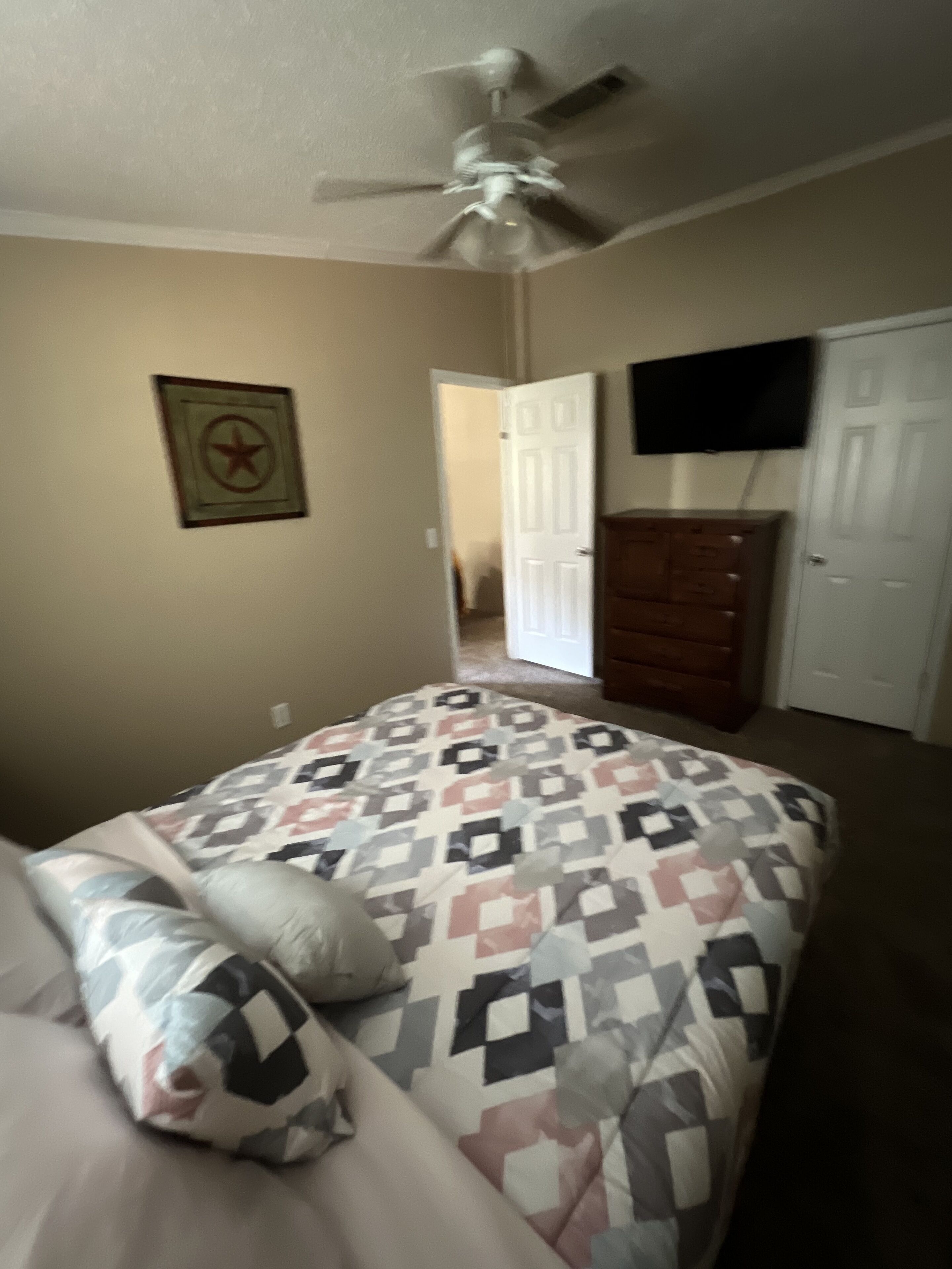 Un dormitorio con cama, cómoda, televisor y ventilador de techo.