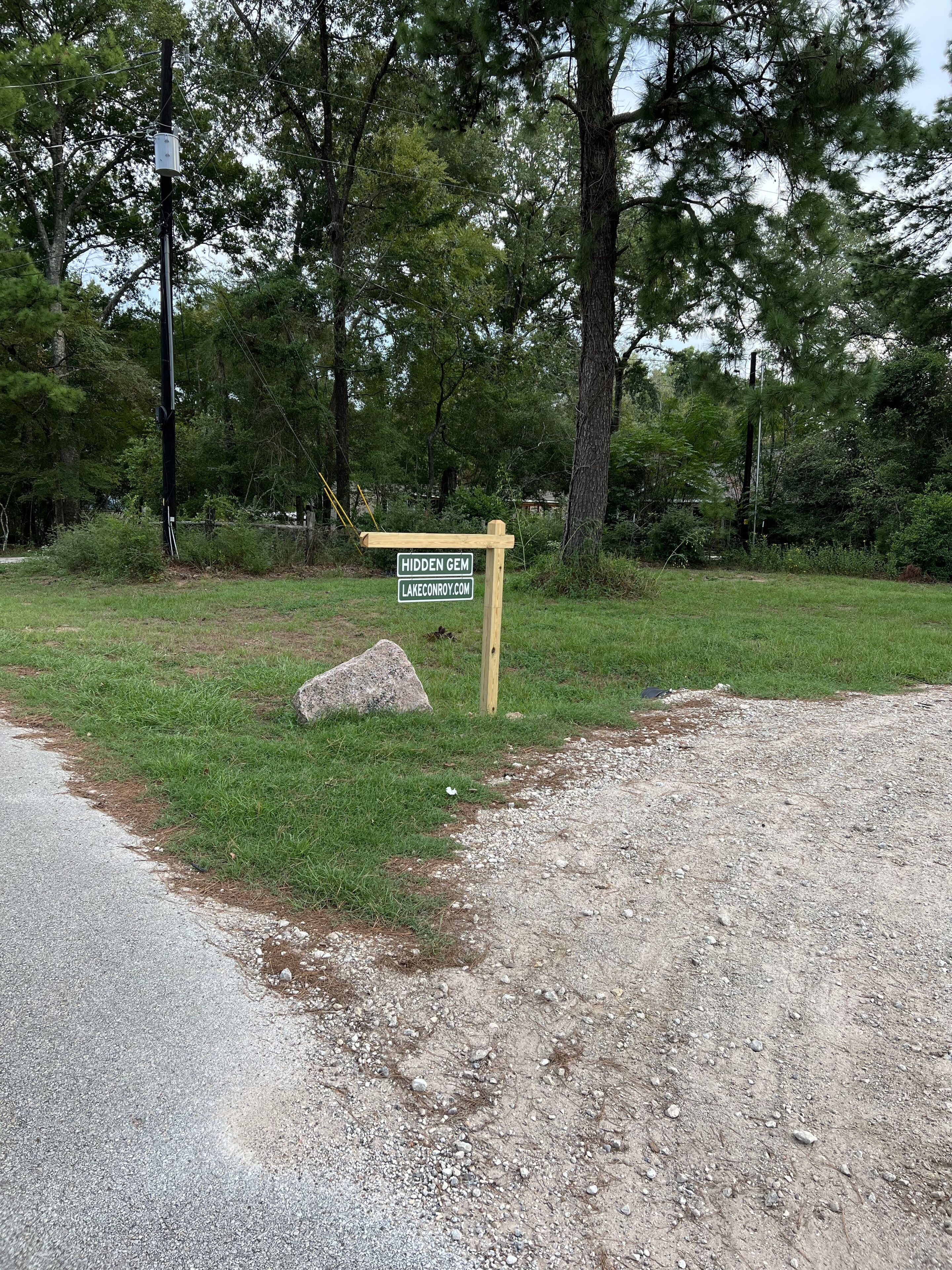 A signpost with 'HIDDEN GEM' and a website address in a natural setting with trees and a gravel path.