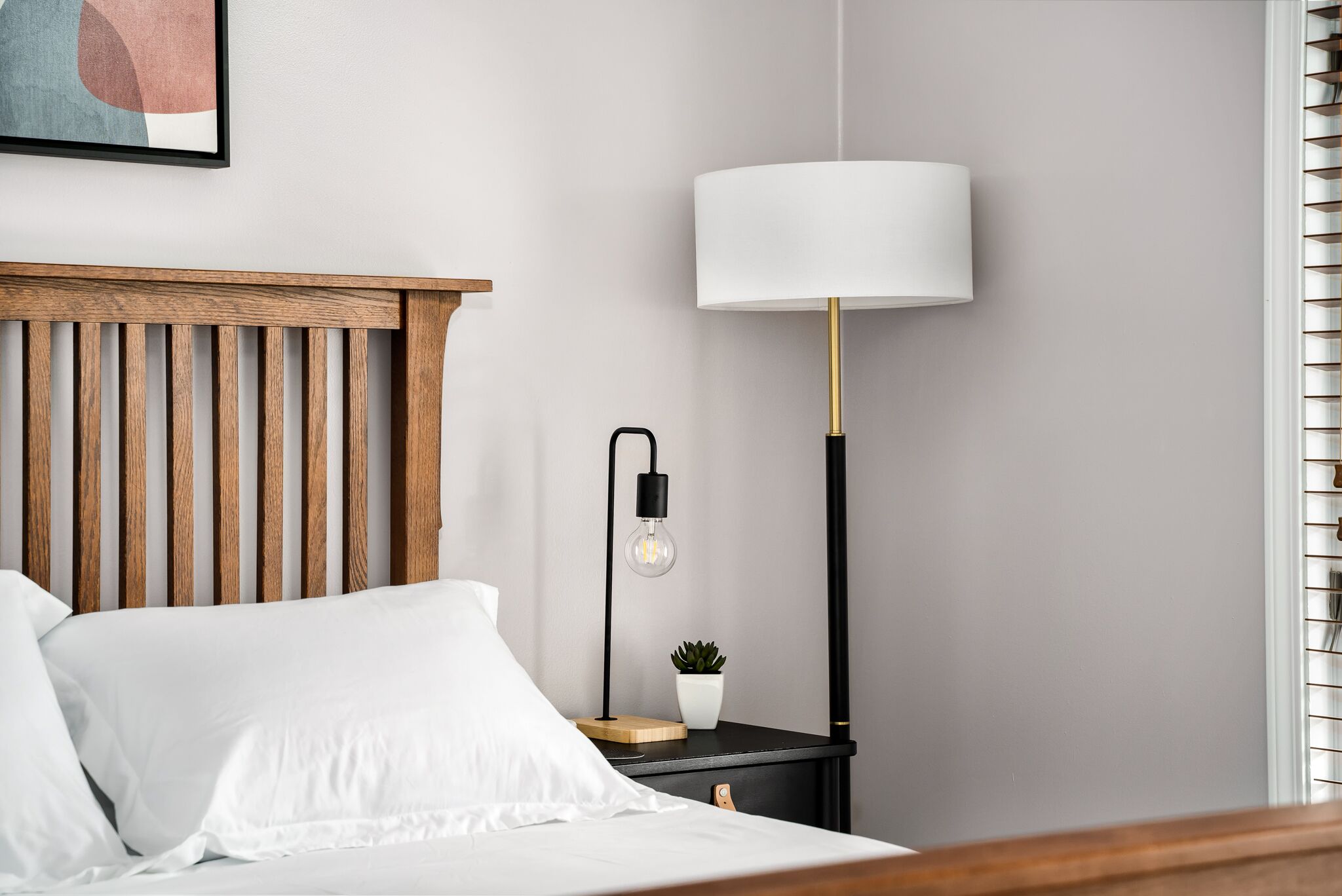A bedroom with a wooden headboard, a bedside lamp, a small potted plant, and a framed picture on the wall.