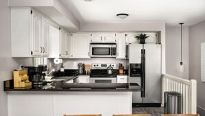 A modern kitchen with white cabinets, a black countertop, stainless steel appliances, and a dining area with a wooden table and chairs. - Mountain cabin near national park & wineries (Linden)