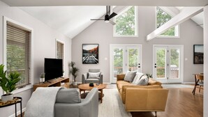 A spacious living room with a high ceiling, large windows, and a flat-screen TV. - Mountain cabin near national park & wineries (Linden)