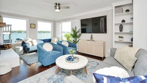A spacious living room with a large window offering a view of the water, a ceiling fan, and a flat-screen TV mounted on the wall. - Luxury Lakefront - Game Room - 7 beds - Hot tub - Kayaks - Dock (Montgomery)