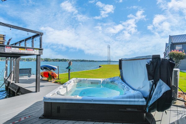 Relax on the deck overlooking the serene body of water, featuring a hot tub and comfortable seating area.