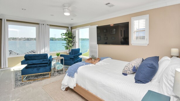 A bedroom with a large bed, a blue chair, a small table, and a view of the water. - Luxury Lakefront - Game Room - 7 beds - Hot tub - Kayaks - Dock (Montgomery)