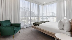 Un dormitorio moderno con una cama grande, un sillón verde y cortinas translúcidas.