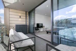 A modern balcony with a glass door leading to a living area, a sofa, and a TV. - Modern & elegant living Wynyard Quarter (Auckland)
