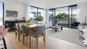 Una sala de estar moderna con comedor, ventanas amplias y vista a un edificio.