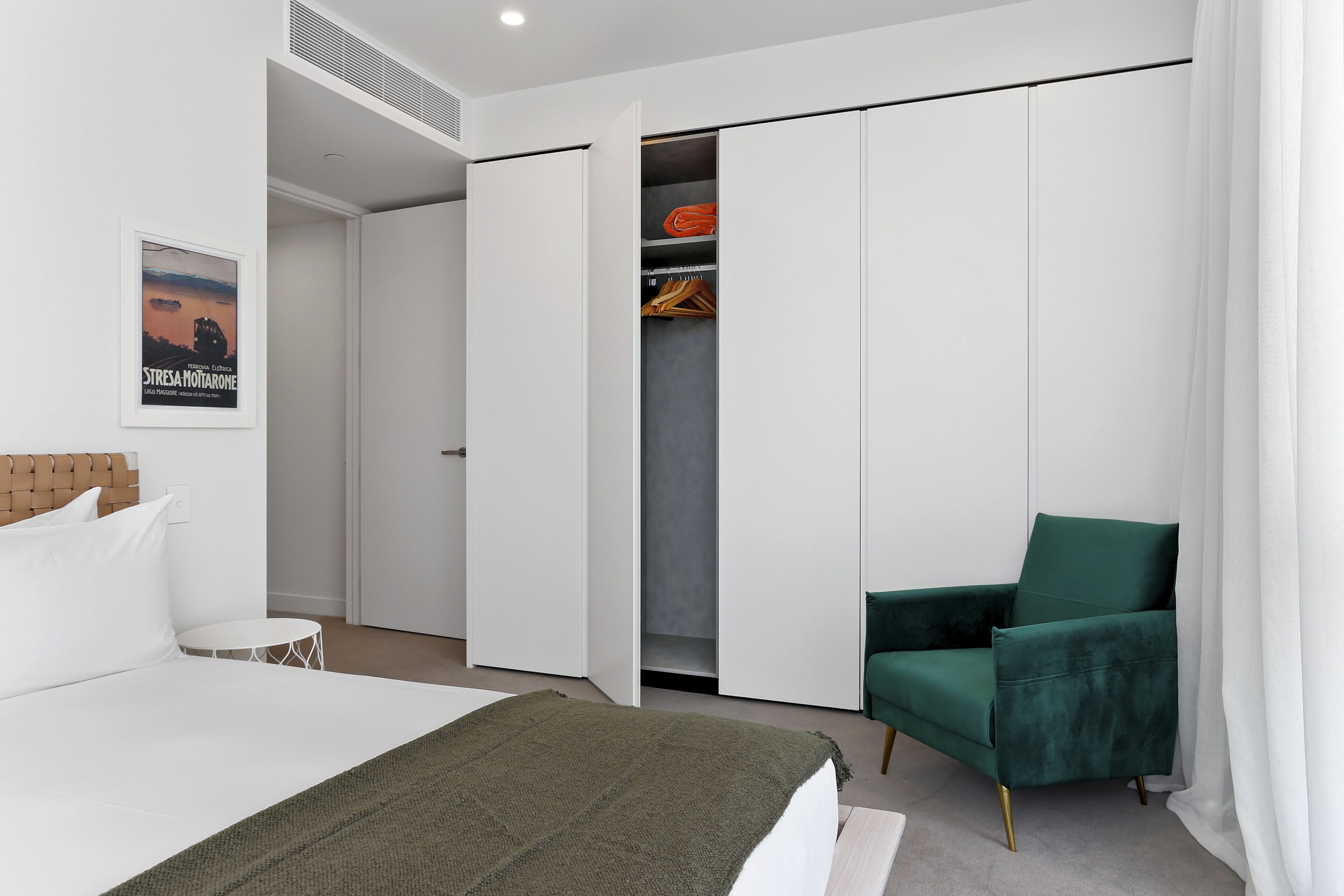 A bedroom with a bed, a green armchair, a wardrobe, and a poster on the wall.