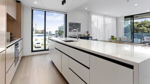 Una cocina moderna con una isla grande, armarios blancos y vistas de la ciudad a través de amplios ventanales.