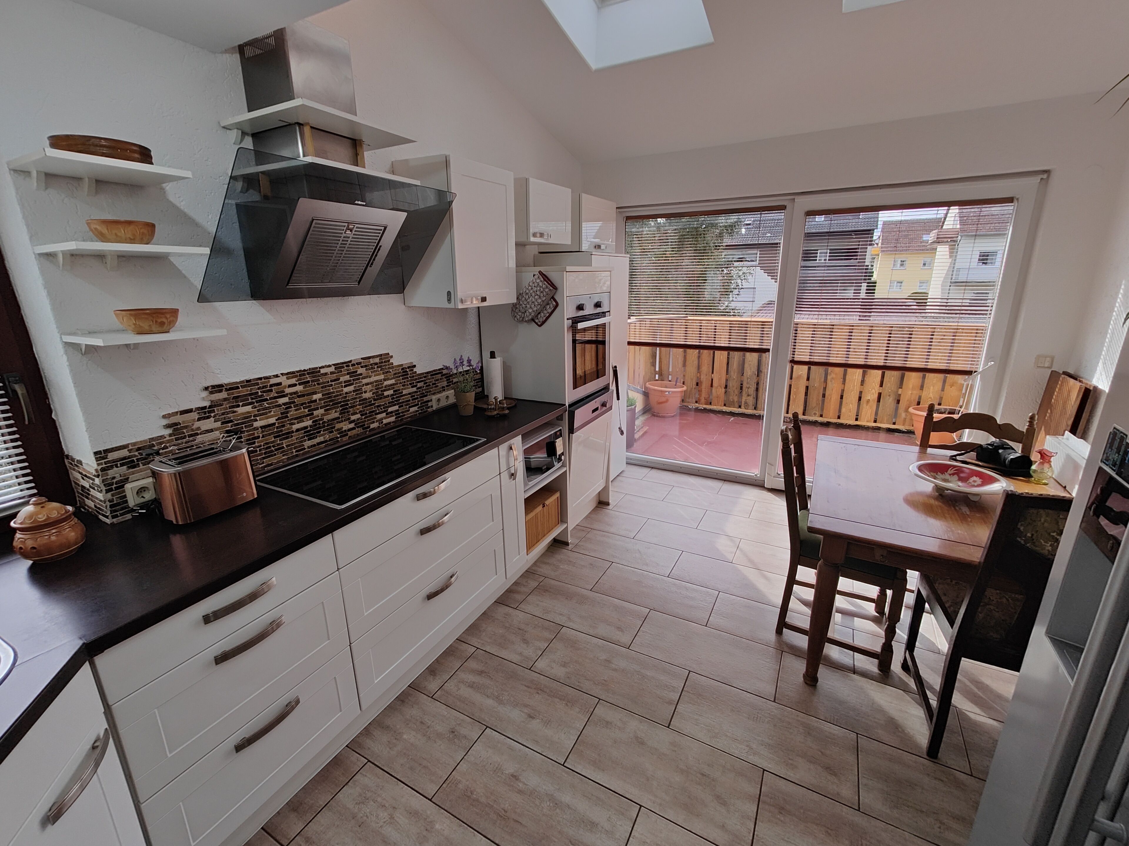 Una cocina moderna con armarios blancos, encimera negra y estufa integrada. Hay una puerta corrediza de vidrio que da a un patio exterior.