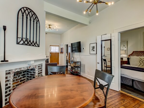 A dining area with a brick fireplace, a round wooden table, and a modern chandelier. - Cottage in Historic District, Heated Pool Access (Savannah)