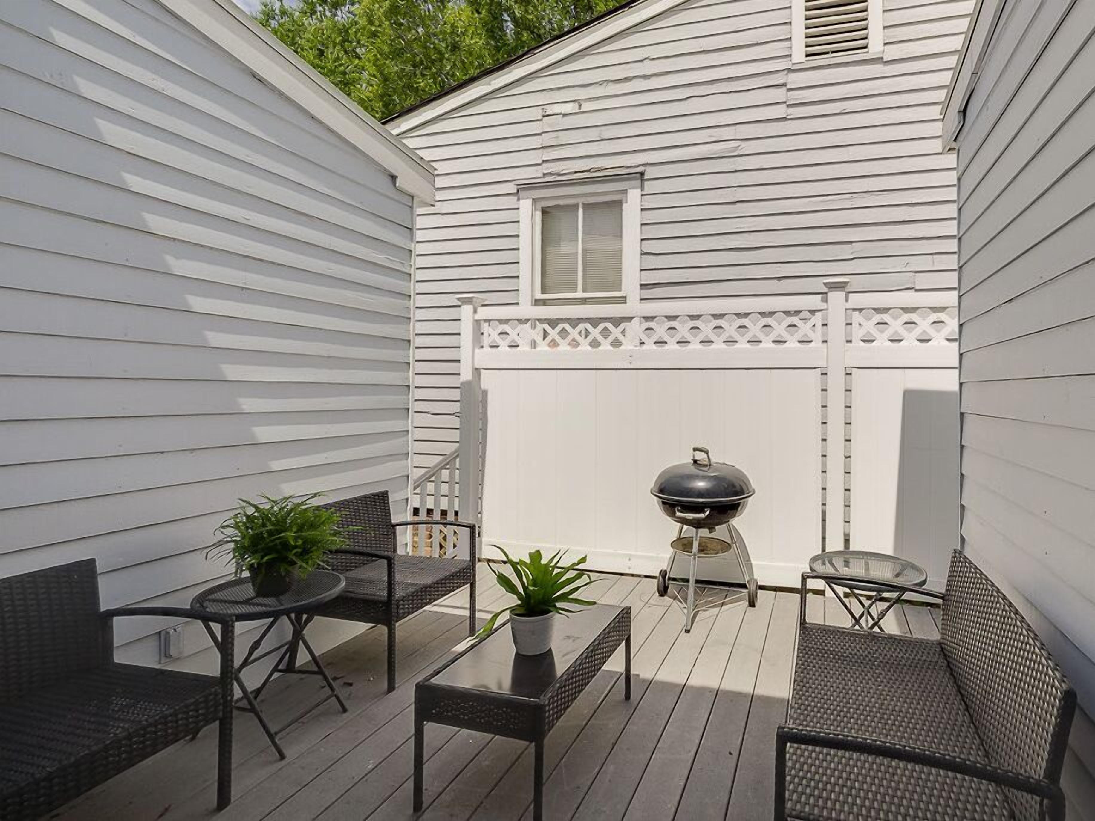 Une terrasse couverte, aménagée avec du mobilier d’extérieur, un barbecue et une clôture blanche.