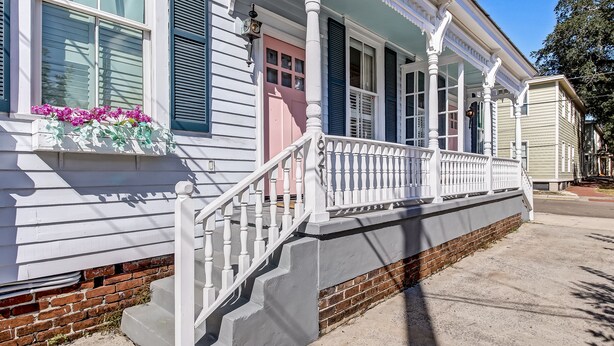 A two-story house with a porch, white railings, and a brick foundation. - Cottage in Historic District, Heated Pool Access (Savannah)