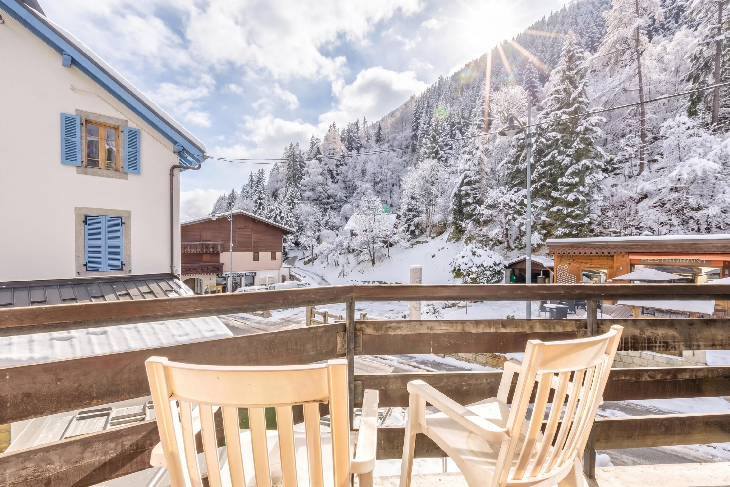 Een balkon met houten stoelen met uitzicht op een besneeuwd berglandschap.