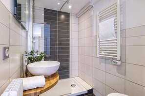 Uma casa de banho moderna com uma grande pia branca, um móvel de banheira de madeira, um box de chuveiro em vidro e um porta-toalhas.