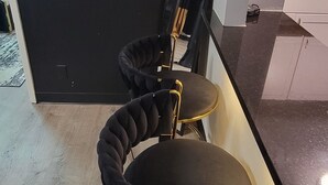 Una zona menjador moderna amb una paret negra, un quadre abstracte daurat i dues cadires tapissades de color negre amb detalls daurats.