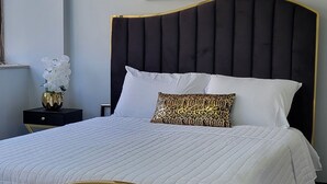 Un dormitori amb un llit tapissat de color negre, roba de llit blanca i un lluminari modern al sostre.