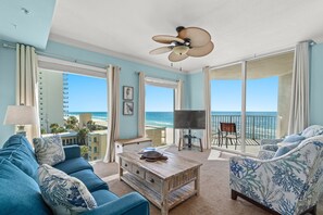 A room with a view of the ocean, a ceiling fan, a wooden coffee table, and a sofa with patterned cushions. - CORNER UNIT 4th floor Beachfront~Panoramic View~walk to Pier Park King BR +Bunks (Panama City Beach)