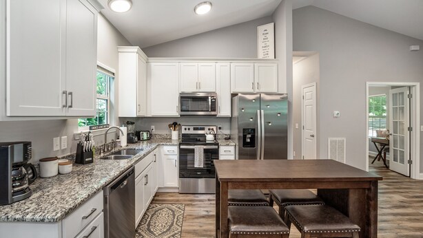 A kitchen with white cabinets, stainless steel appliances, a granite countertop, and a wooden dining table with benches. - Cozy House in the Woods - 25 minutes from downtown (Pegram)