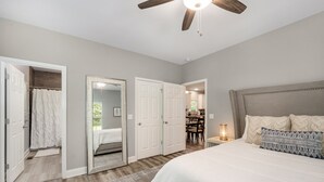 A bedroom with a large bed, a ceiling fan, and a view into the kitchen. - Cozy House in the Woods - 25 minutes from downtown (Pegram)