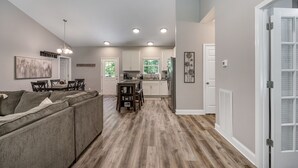 A spacious living area with a sofa, dining table, and kitchen in the background. - Cozy House in the Woods - 25 minutes from downtown (Pegram)
