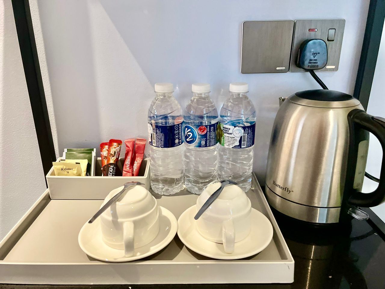 A tray with two white sugar bowls, three water bottles, and a silver kettle on a countertop.