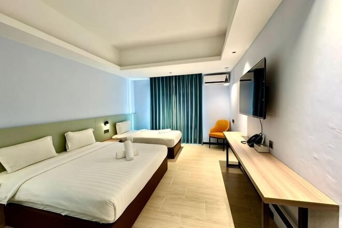 A hotel room with two beds, a desk, a chair, a flat-screen TV, and a window with curtains.