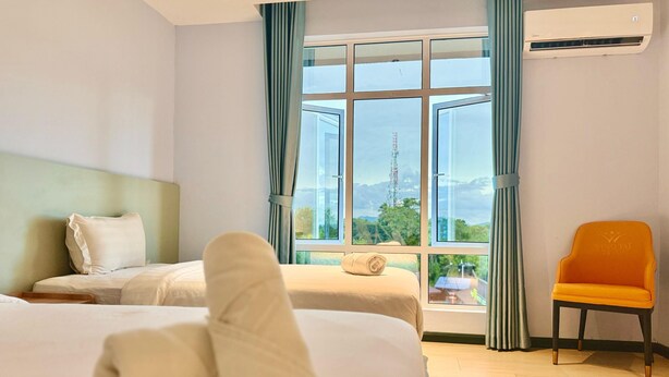 A hotel room with two beds, a view of the outdoors, and an air conditioning unit. - Wing Tat Grand Hotel (Semporna)