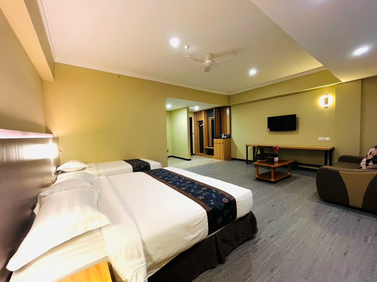 A hotel room with two beds, a desk, a television, and a ceiling fan.