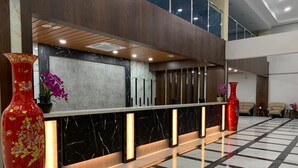 A reception area with a marble counter, two large red vases, and a checkered floor. - Wing Tat Grand Hotel (Semporna)