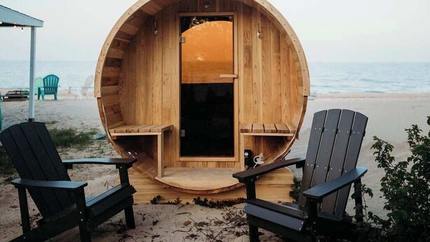 Una cabaña de madera con diseño circular, dos sillas Adirondack y vista al mar.