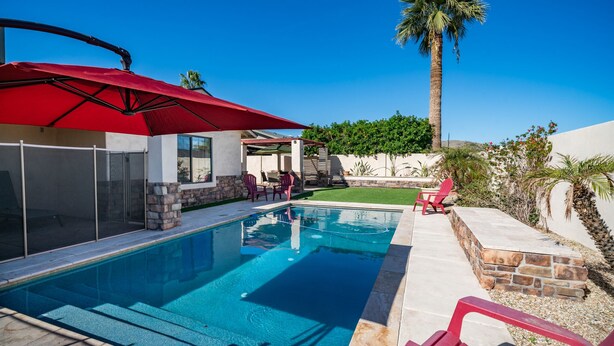 A swimming pool with a red umbrella, stone walls, and a view of a palm tree. - South Mountain Retreat - Free Heated Pool, Tesla outlet, RV Parking (Phoenix)