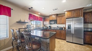 A kitchen with a central island, wooden cabinets, stainless steel appliances, and a window with red curtains. - South Mountain Retreat - Free Heated Pool, Tesla outlet, RV Parking (Phoenix)