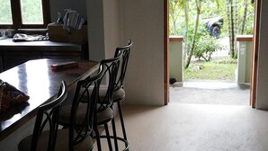 Una habitación con comedor, que incluye una mesa y sillas, una ventana con cortinas y una puerta abierta que da a un jardín con palmeras.