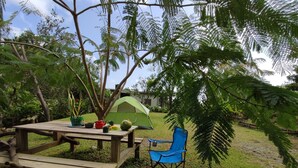 Una mesa de picnic de madera con una tienda verde y una silla azul en un área cubierta de césped y árboles.