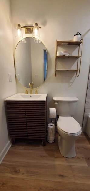 Ein Badezimmer mit einem Holzkosmetikschrank, einem runden Spiegel, einer Toilette und einem Ablagefach für Toilettenartikel.