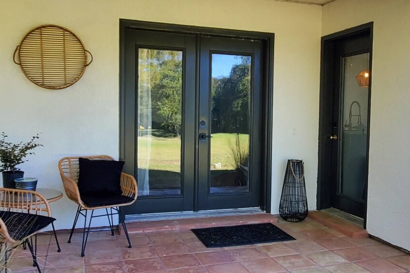 Un espace patio avec une porte noire, une chaise en osier, une petite table et une plante en pot.