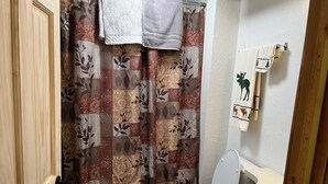 Kylpyhuone, jossa on kukkakuviollinen suihkuverho, wc ja pesuallas, ja seinällä on pyyhe.