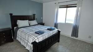 Un dormitorio con una cama, una mesita de noche, un ventilador de techo y una ventana con cortinas.