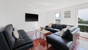 Una sala de estar moderna con un sofá de cuero negro, una mesa de centro de madera y un televisor de pantalla plana montado en la pared.