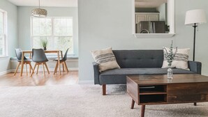 Un salon avec un canapé gris, une table basse en bois et un coin repas comprenant une table et des chaises.
