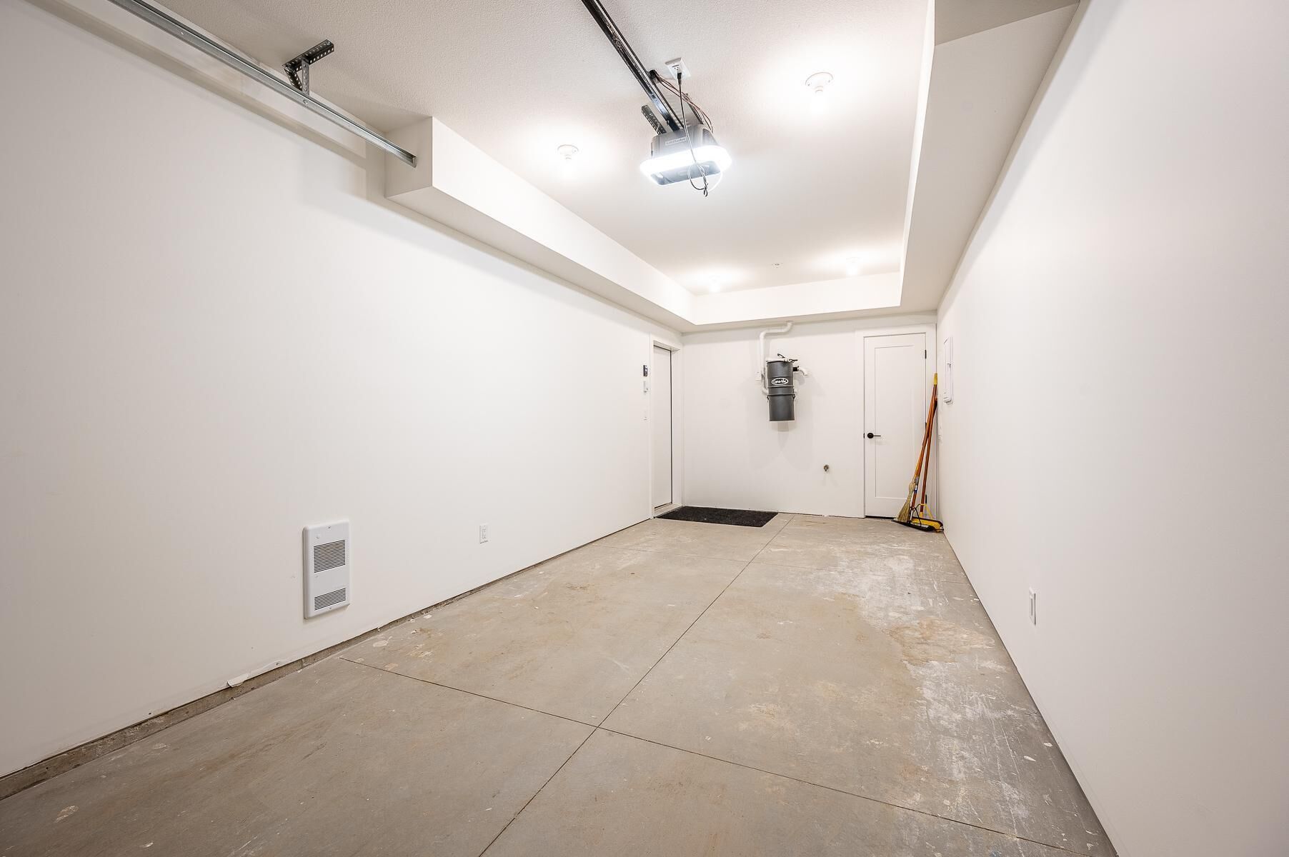 Une pièce propre et vide, avec des murs blancs, un sol carrelé, un projecteur fixé au plafond et une porte avec un paillasson.