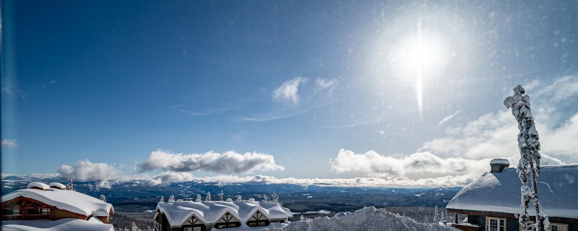 Un albergue de montaña cubierto de nieve con varias construcciones de estilo chalet, una torre destacada y vistas despejadas de las montañas circundantes.